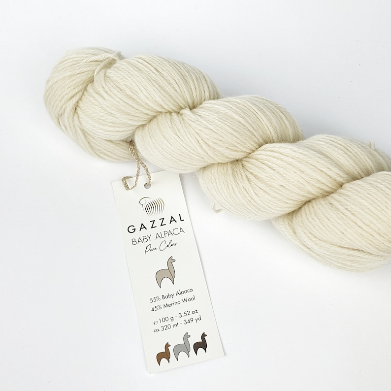 May include: A skein of cream-coloured yarn labelled "GAZZAL BABY ALPACA Pure Colors" with a label that reads "55% Baby Alpaca 45% Merino Wool  ~100 g - 3.52 oz  ca 320 mt - 349 yd".