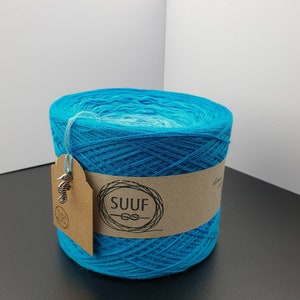 May include: A skein of turquoise blue yarn with a white ombre effect. The yarn is wrapped around a cardboard tube with a brown paper label that says "SUUF" with a knot symbol. A silver seahorse charm is attached to the label.