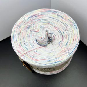 May include: A white ball of yarn with multi-coloured speckles of pink, blue, green, and yellow. The yarn is wound around a cardboard tube with a label that says "SHUF".