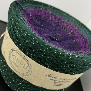 May include: A skein of green, purple, and pink yarn with gold glitter. The yarn is wound into a ball and has a brown label with the text "KHIPU" and "Anna Sakovska" on it.
