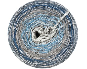 Puede incluir: Un ovillo de hilo en un degradado de colores azul, gris y plateado. El hilo está enrollado en forma de bola y está listo para tejer o hacer ganchillo.