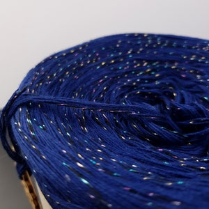 May include: A close-up of a blue yarn with gold, silver, and pink glitter threads woven throughout.