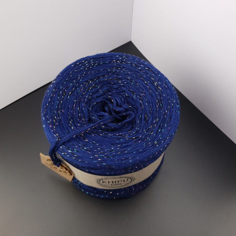 May include: A skein of navy blue yarn with iridescent glitter threads. The yarn is wound into a ball and has a label that says "KHIPU".
