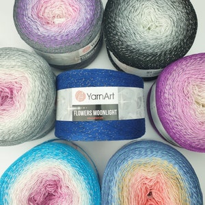 May include: Assortment of six yarn skeins in various color gradients, including pink, blue, gray, and purple. Each skein features a subtle shimmer and is labeled "YarnArt Flowers Moonlight" with the website address "www.yarnart.info".