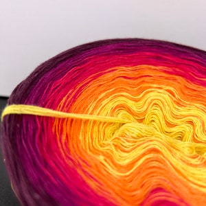 May include: A skein of yarn with a gradient of colors from dark purple to yellow. The yarn is wound into a ball shape.