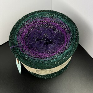 May include: A skein of green, purple, and gold yarn with glitter. The yarn is wound into a ball and has a label that says "KHIPU".