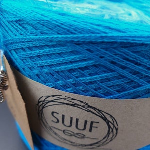May include: A close-up of a bright blue ball of yarn with a brown label that says "SUUF" in a circle.