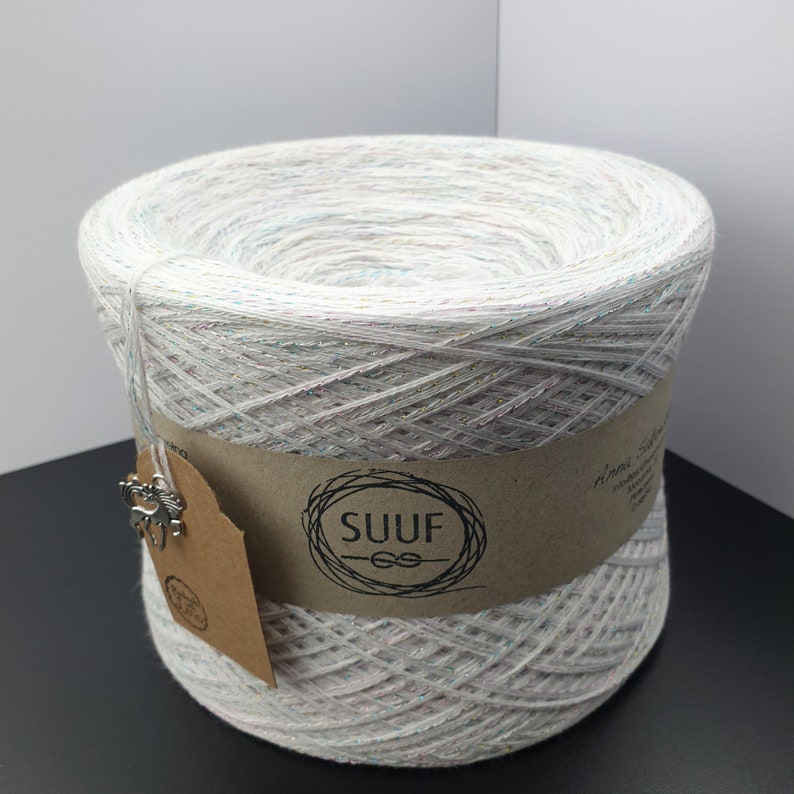 May include: A white yarn skein with iridescent glitter threads. The yarn is wrapped around a brown cardboard tube with a label that says "SUUF" in a black circle.