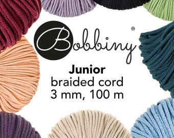 May include: Assortment of colorful braided cotton cords in various colors, including red, purple, beige, green, blue, and black. The cords are arranged in a circle around the text "Bobbiny Junior braided cord 3 mm, 100 m".