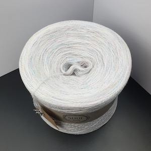 May include: A white yarn skein with multi-colored flecks. The yarn is wound around a cardboard tube with a brown label that says "SUUF."