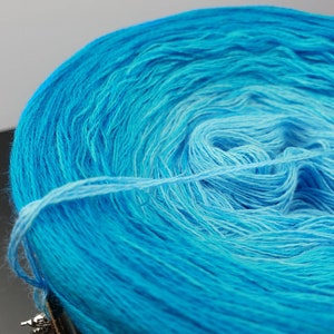 May include: A skein of yarn in a gradient of blue shades, from a light blue to a darker blue. The yarn is wound into a ball shape.