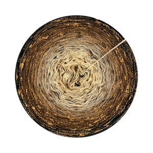 May include: A circular skein of yarn with a gradient of colors, transitioning from a dark brown outer edge to a light beige center. Gold flecks are interspersed throughout the yarn, and a single strand of yarn extends from the center.