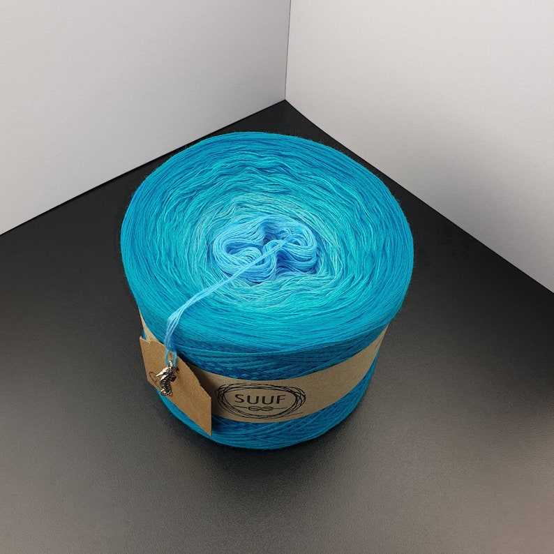 May include: A skein of blue ombre yarn wound into a ball with a brown paper label that says "SUUF" with a knot design.