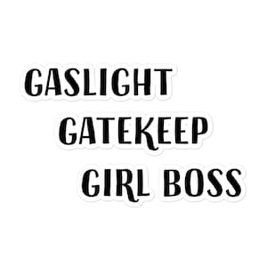 以下が含まれることがあります： 白地に黒と白のテキスト。テキストは「Gaslight Gatekeep Girl Boss」です。
