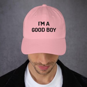 May include: A pink baseball cap with black embroidered text that reads "I'M A GOOD BOY".