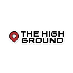 Op de afbeelding: Een sticker met een gepixelde afbeelding van een rode locatiepin en de tekst "THE HIGH GROUND" in zwart.