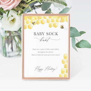 May include: A printable baby shower game card with a honeycomb pattern and bees. The text reads "BABY SOCK hunt. There are 10 pairs of baby socks hidden throughout the shower. Whoever finds the most pairs wins a prize! Happy Hunting!"