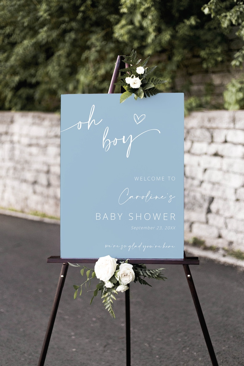 Pode incluir: Uma placa de boas-vindas azul claro com caligrafia branca que diz "oh boy" com um pequeno cora&ccedil;&atilde;o acima da palavra "boy". A placa tamb&eacute;m inclui o texto "Welcome to Caroline's Baby Shower September 23, 20XX we're so glad you're here".