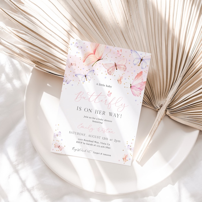Puede incluir: Una invitaci&oacute;n de baby shower rosa y dorada con un dise&ntilde;o de mariposa. La invitaci&oacute;n dice "&iexcl;Un peque&ntilde;o beb&eacute; mariposa est&aacute; en camino!" e incluye la fecha, la hora y el lugar de la ducha. Tambi&eacute;n dice "RSVP a Sarah al 123.456.7890".