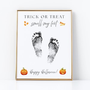 May include: A rectangular framed print with a white background featuring the black text TRICK OR TREAT smell my feet and Happy Halloween. The design includes two black baby footprints in the center, orange candy corn, and two orange jack-o'-lanterns.