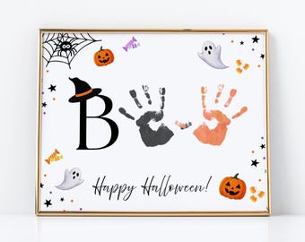 May include: A framed Halloween print featuring a large black letter B wearing a witch hat, a black handprint, and an orange handprint. The white background includes illustrations of ghosts, pumpkins, a spider web, and the text Happy Halloween.