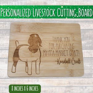 May include: A rectangular bamboo cutting board with a goat illustration and the text "THANK YOU FOR PURCHASING MY FFA MARKET GOAT! - Kendall Craft." The board measures 8 inches by 6 inches.