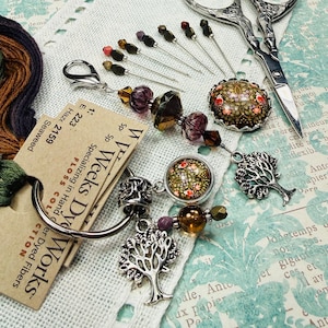 May include: A collection of craft items, including embroidery floss, needles, decorative beads, and scissors. The floss is in shades of green, brown, and purple. The image includes a tag that reads "Weeks Dye Works".