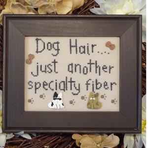 May include: A framed cross-stitch design with the text "Dog Hair... just another specialty fiber". The design features two dogs, one black and white and one brown, with paw prints and bone-shaped buttons.