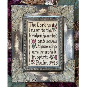 May include: A framed cross-stitch with a religious quote: "The Lord is near to the brokenhearted and saves those who are crushed in spirit Psalm 34:18". The frame is ornate and has a distressed, aged look.