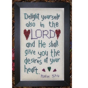 May include: A framed cross-stitch with the text "Delight yourself also in the LORD and He shall give you the desires of your heart.. PSALM 37:4". The text is in a green and purple font with red hearts.