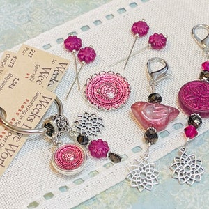 Könnte beinhalten: Ein Set aus rosa und silbernen Nadelhaltern und eine Schere. Die Nadelhalter haben ein Mandala-Design und sind an einer silbernen Kette mit einem silbernen Ring befestigt. Die Schere hat einen silbernen Griff und eine schwarze Klinge. Der Text auf dem Etikett lautet "Weeks Weeks Live Works Specializing in Hand-Dyed Fibers Over Dyed Fibers Collection Cotton 5 yards 1343 Boysenberry Grape Vine 1273 227 Ron"