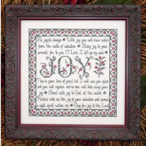 May include: Framed cross-stitch artwork with the word "JOY" in the center, surrounded by floral accents and text. The frame is dark red with ornate detailing. The text includes inspirational phrases.