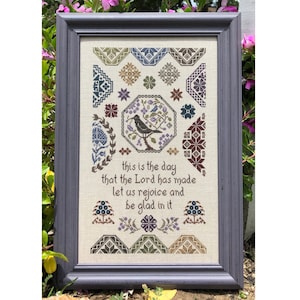 Puede incluir: Un sampler de punto de cruz enmarcado con un diseño de pájaro y flores. El sampler incluye el texto "this is the day that the Lord has made let us rejoice and be glad in it".