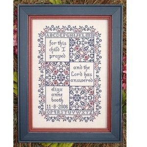 Puede incluir: Un sampler de punto de cruz enmarcado con un borde floral. El sampler presenta el texto "for this child I prayed and the Lord has answered" y el nombre "eliza anne booth" con la fecha "11-8-2006".