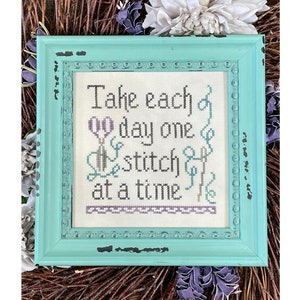 May include: A framed cross-stitch with the quote "Take each day one stitch at a time" in a teal frame.