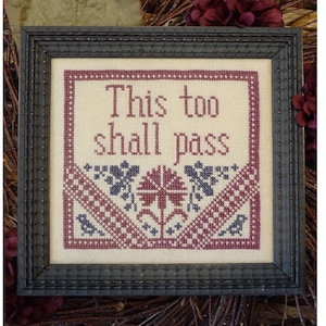 Può includere: Un ricamo a punto croce incorniciato con la frase "This too shall pass" in lettere bordeaux. Il ricamo presenta un motivo floreale rosso e blu con un bordo bordeaux e bianco.