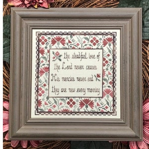 May include: A framed cross-stitch with a floral border and the text "the steadfast love of the Lord never ceases His mercies never end they are new every morning".