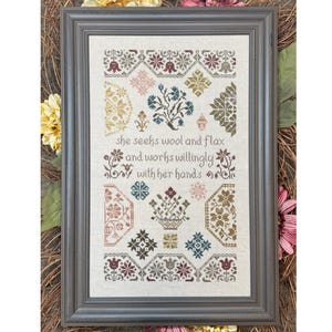Könnte beinhalten: Ein gerahmter Kreuzstich-Sampler mit einem floralen Design und dem Text "Sie sucht Wolle und Flachs und arbeitet willig mit ihren Händen."