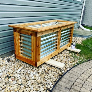 Puede incluir: Una jardinera de madera con un revestimiento de metal. La jardinera est&aacute; hecha de madera natural y tiene un aspecto r&uacute;stico. El revestimiento de metal es corrugado y tiene un acabado plateado. La jardinera est&aacute; sentada sobre un lecho de peque&ntilde;as piedras.