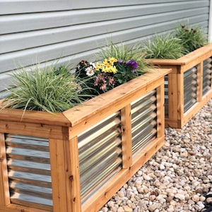 Puede incluir: Dos jardineras de madera con paneles de metal corrugado y una variedad de flores en flor. Las jardineras est&aacute;n sentadas sobre un lecho de peque&ntilde;as piedras blancas.