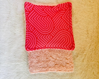 Könnte beinhalten: Ein wiederverwendbarer Gesichtsschwamm in zwei Farbtönen. Der obere Teil hat ein leuchtend rotes geometrisches Muster auf rosa Grund. Der untere Teil besteht aus weichem, pfirsichfarbenem Plüschmaterial. Der Schwamm ist für sanftes Peeling und Reinigung konzipiert.