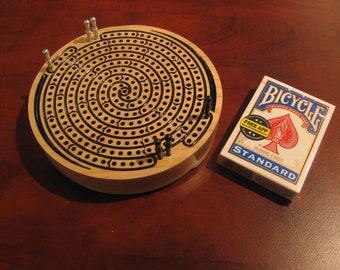 May include: A wooden spiral peg game with silver pegs and a deck of Bicycle playing cards. The cards have a blue and white design with the text "Bicycle Trusted Since 1885 Playing Cards Standard".