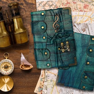 May include: An assortment of nautical and travel-themed items on a wooden surface. Includes a pair of brass binoculars, a compass, a small sailboat, and two teal leather journals with brass accents. The journals feature a treble clef and a clasp.