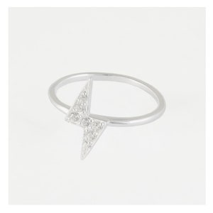 Peut inclure: Une bague en argent avec un motif d'éclair. L'éclair est orné de petites pierres précieuses claires. La bague a un anneau fin et une finition polie, sur fond blanc.