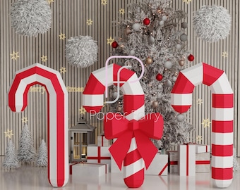 Pode incluir: Três grandes bengalas de papel listradas de vermelho e branco com um laço vermelho em uma. As bengalas estão em pé na frente de uma árvore de Natal com luzes brancas e enfeites vermelhos e prateados. O fundo é uma parede de painéis de madeira com bolas brancas e fofas penduradas na parede.