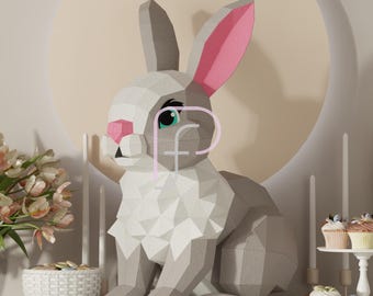 May include: A gray and white papercraft bunny with pink ears and blue eyes. The bunny is sitting on a table with a basket of flowers, candles, and cupcakes.