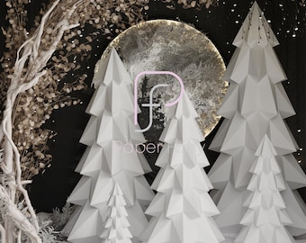 May include: Four white paper Christmas trees of varying sizes, with a large, round, gold and white moon behind them. The trees are made of folded paper and have a geometric design. The background is black with white snowflakes.