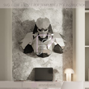 May include: A silver and black papercraft model of a Predator head, mounted on a gray wall. The model is made of many small triangles, giving it a polygonal appearance. The Predator's face is visible, with its iconic mandibles and red eyes. The model is a popular choice for fans of the Predator franchise.