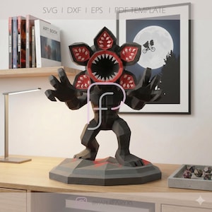 May include: A black and red papercraft Demogorgon figure with a detailed, open-mouthed head and outstretched arms. The figure is on a gray, geometric base with red accents. The image includes text at the top: SVG | DXF | EPS | PDF TEMPLATE.