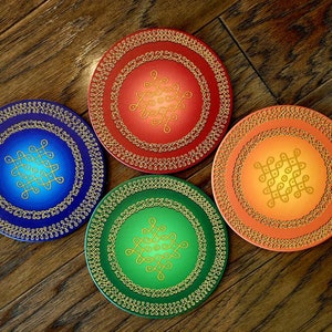 May include: Four round decorative plates with a gold mandala design on a wood background. The plates are blue, green, orange, and red.